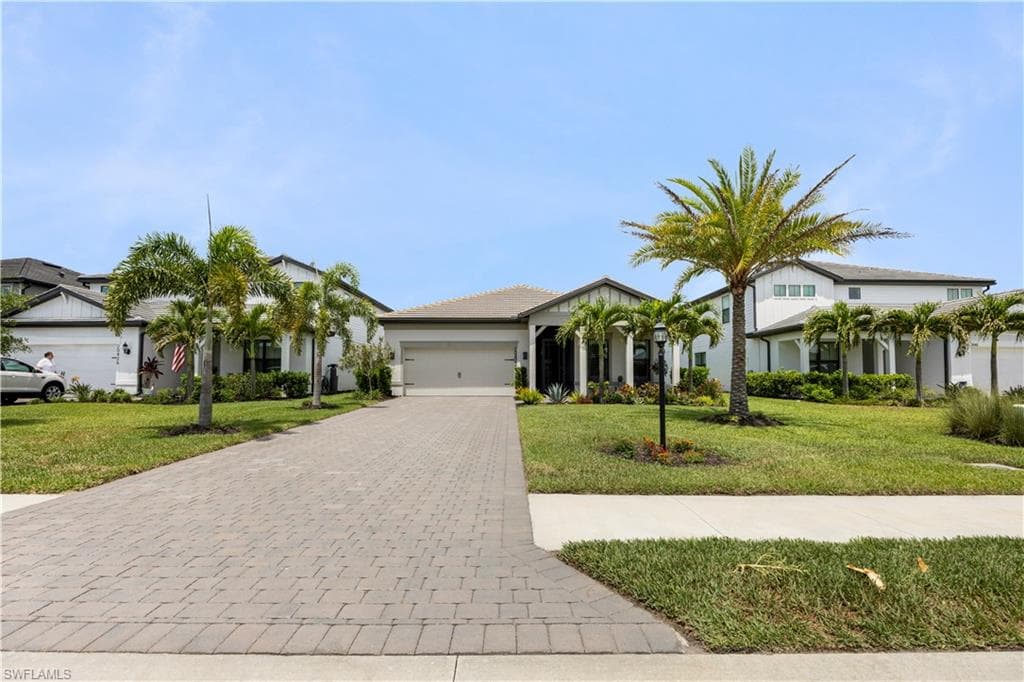 Contemporary single-story residence with a paver driveway, manicured lawn, multiple palm trees, and a two-car garage