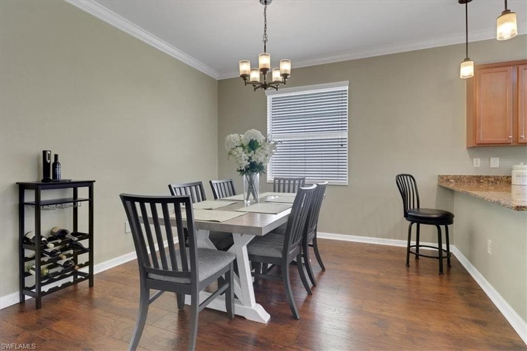 Dining space featuring baseboards, ornamental molding, a notable chandelier, and dark wood-style flooring