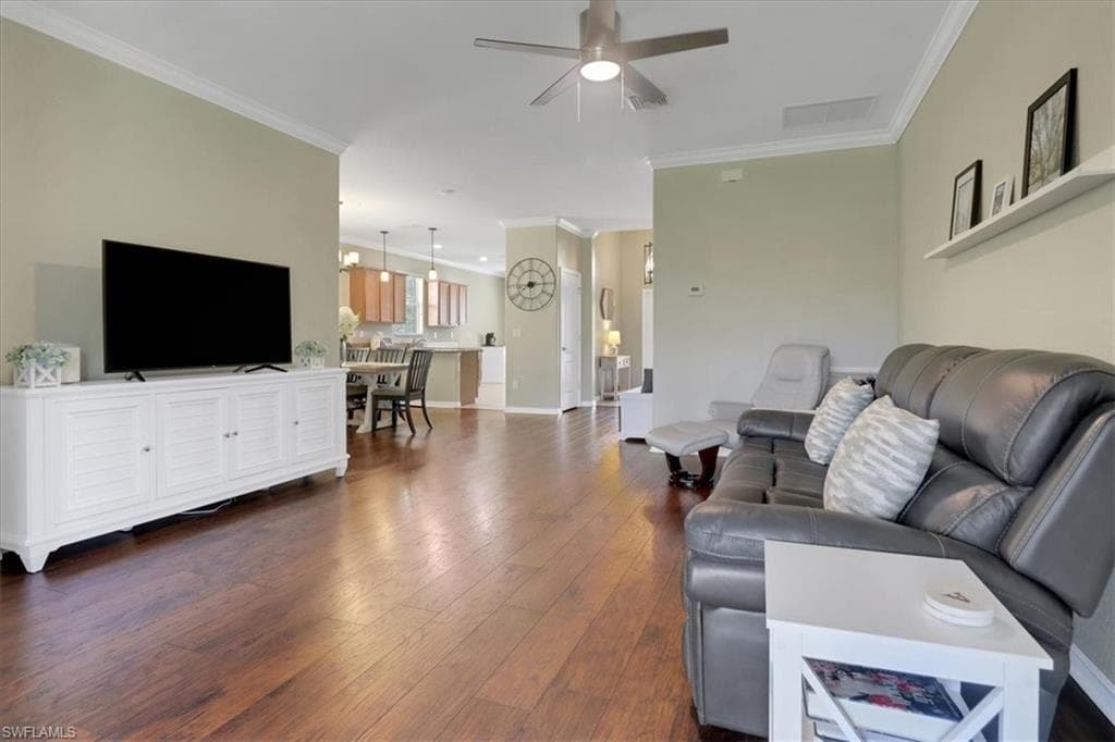 Living room with crown molding, dark wood-style floors, a ceiling fan, and visible vents