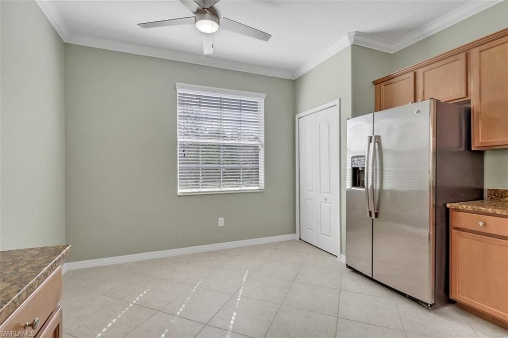 Kitchen featuring stainless steel fridge, crown molding, ceiling fan, dark stone counters, and wood finish cabinetry