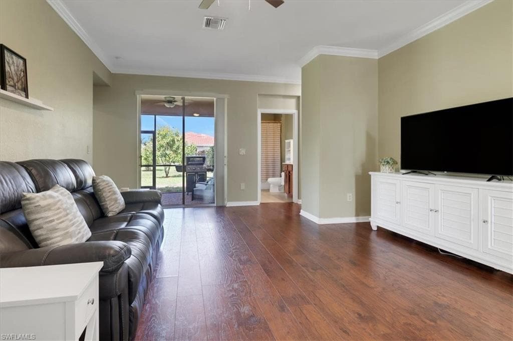 Living room featuring dark wood finished floors, visible vents, ornamental molding, and ceiling fan