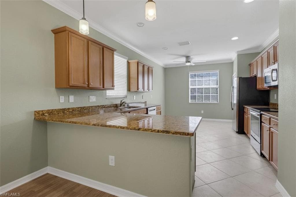Kitchen featuring a peninsula, stainless steel appliances, wood finish cabinets, dark stone countertops, and ornamental molding