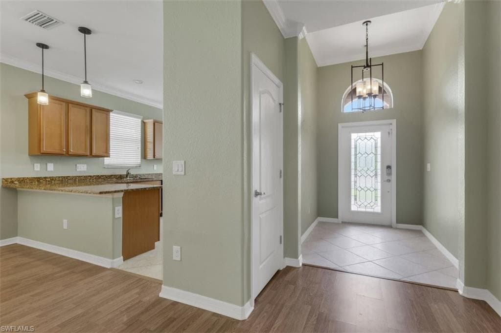 Foyer entrance with crown molding, a chandelier, and light wood-style floors