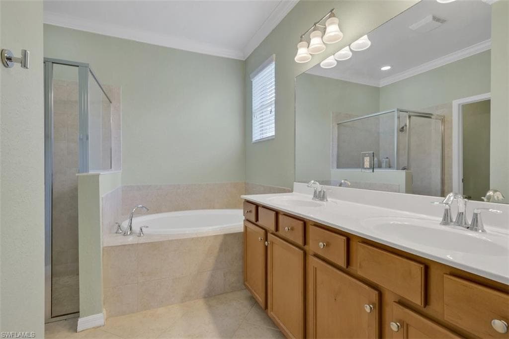 Bathroom featuring double vanity, ornamental molding, a garden tub, a stall shower, and light tile patterned floors