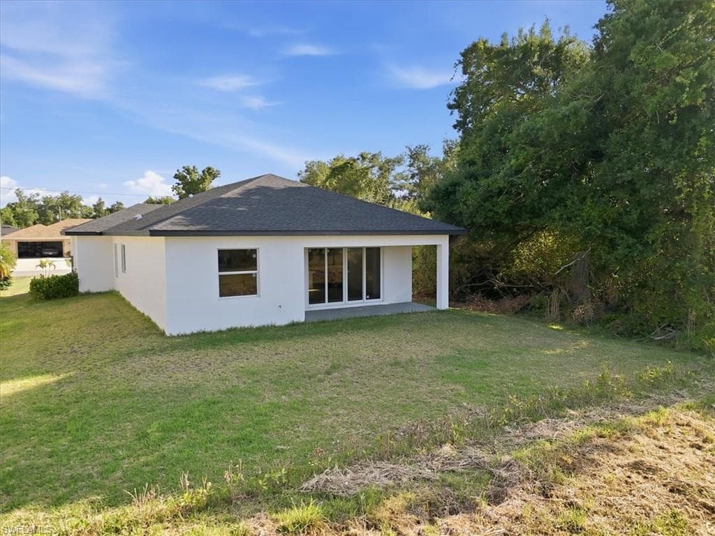 Rear exterior featuring a white stucco finish, dark shingle roof, and a covered patio area