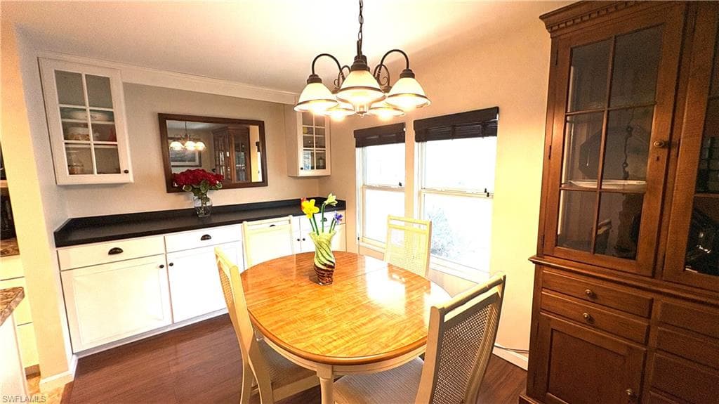 Dining area has a wood-finish flooring, multi-light chandelier, built-in buffet, dark countertops, and upper glass-front cabinets.