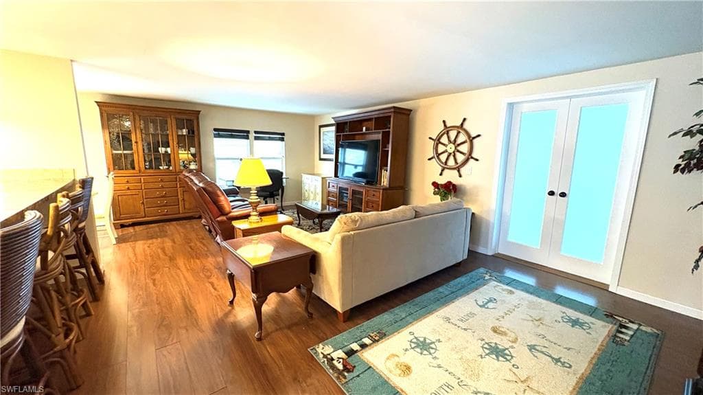 Expansive living area has beautiful wood-finish flooring, white baseboards, and light-toned walls. The double doors lead to the air-conditioned Florida Room.