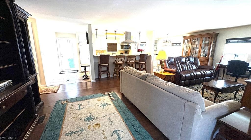 Open-concept living room with view to the entry. You’ll love the rich wood-finish flooring, kitchen island with pendant lighting, stainless steel range hood, and recessed lighting.