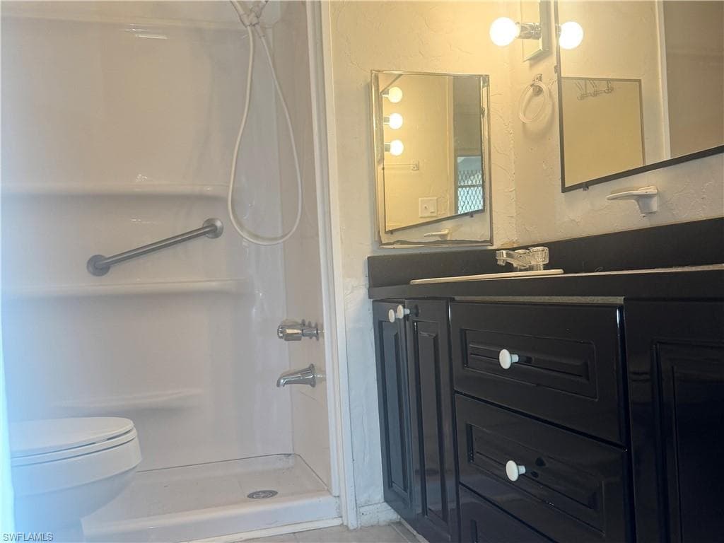 Bathroom featuring a white shower stall with an integrated grab bar, a white toilet, and a black vanity with a contrasting white countertop
