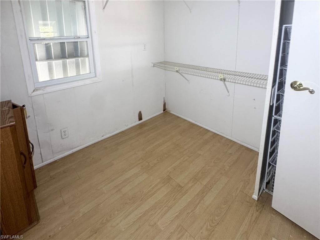 Room featuring light wood-finish flooring, a double-hung window with blinds, and built-in wire shelving