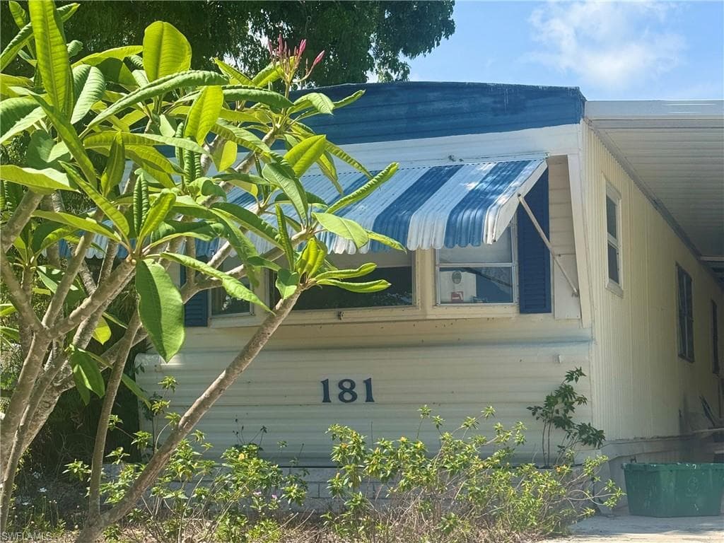 Siding exterior featuring a striped fabric awning, white-framed windows, and dark louvered shutters