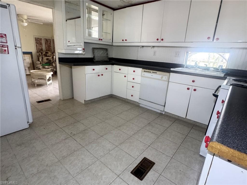 Kitchen featuring white cabinetry with red knobs, dark countertops, a built-in dishwasher, and a window above the sink