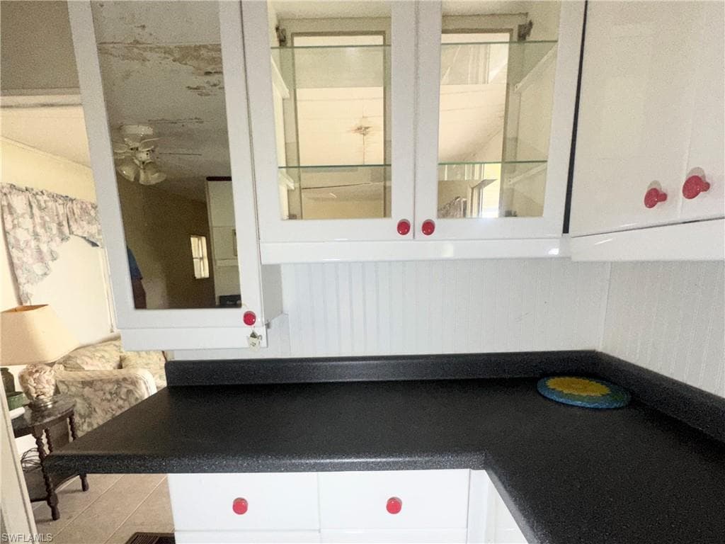 White cabinetry with red knobs, dark countertops, glass-front upper cabinets, and a white beadboard backsplash