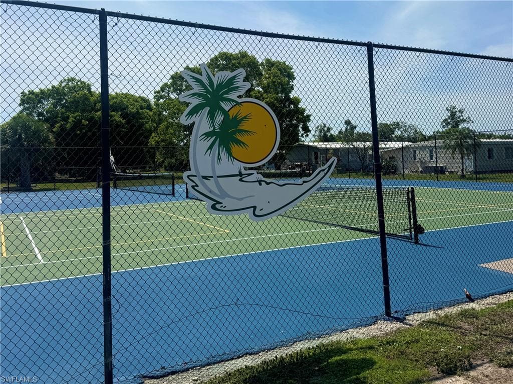 Fenced tennis court featuring a blue playing surface with green court lines and a net