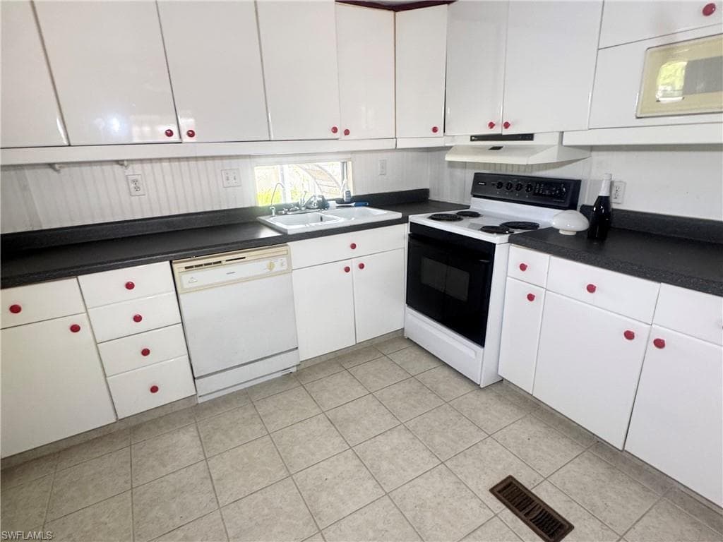 Kitchen featuring white cabinetry with red hardware, dark countertops, and tile flooring