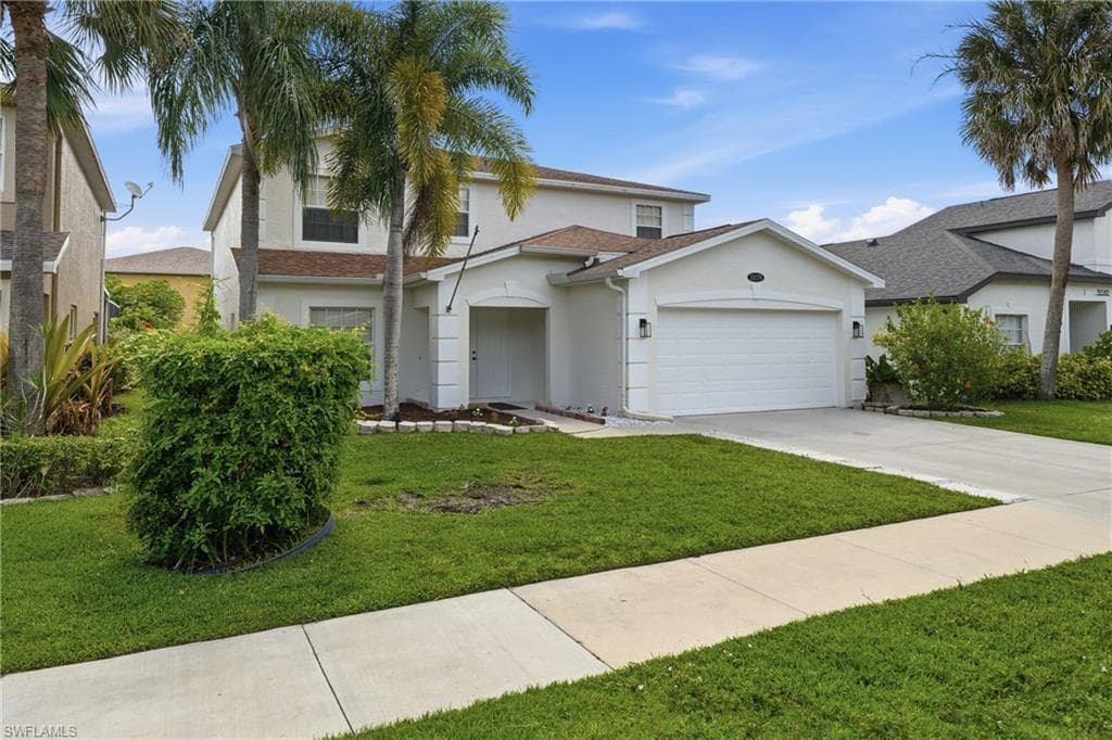 Two-story residence featuring a white stucco exterior, an attached two-car garage, concrete driveway, front yard with mature landscaping, and an inviting covered entry