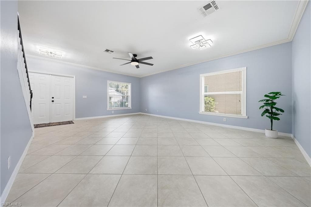 Spacious interior featuring light-colored tile flooring, light blue walls, white baseboards, and crown molding