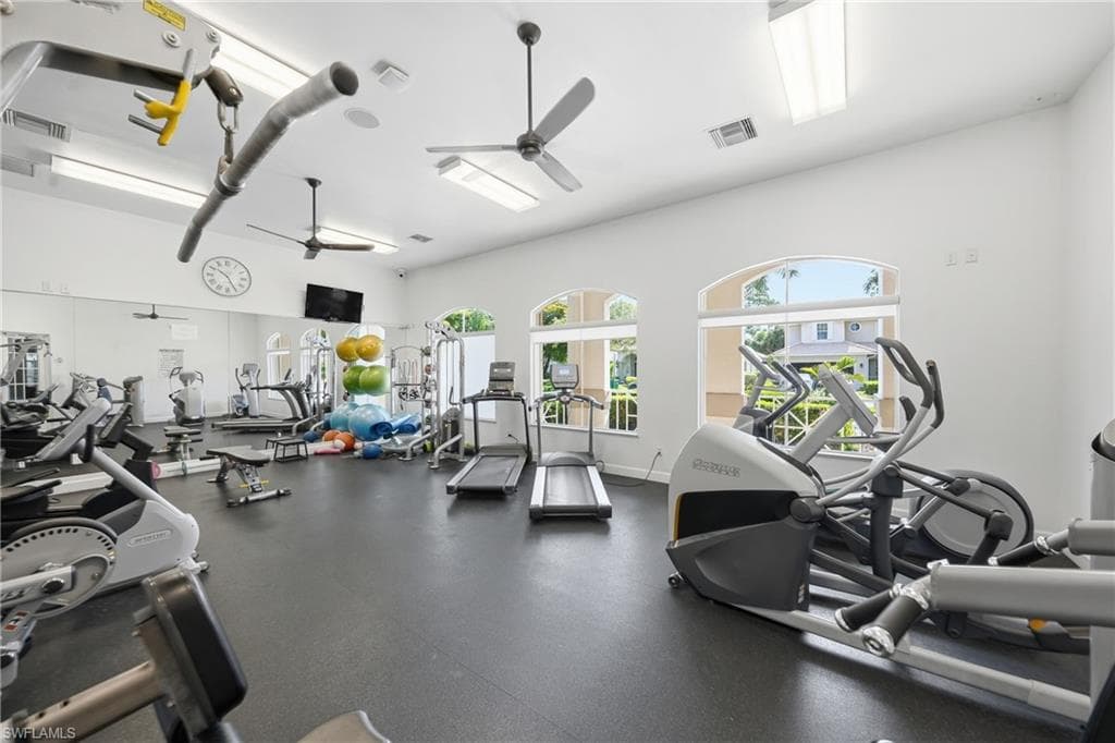 Fitness center featuring ample natural light from arched windows, dark rubber flooring, and multiple ceiling fans