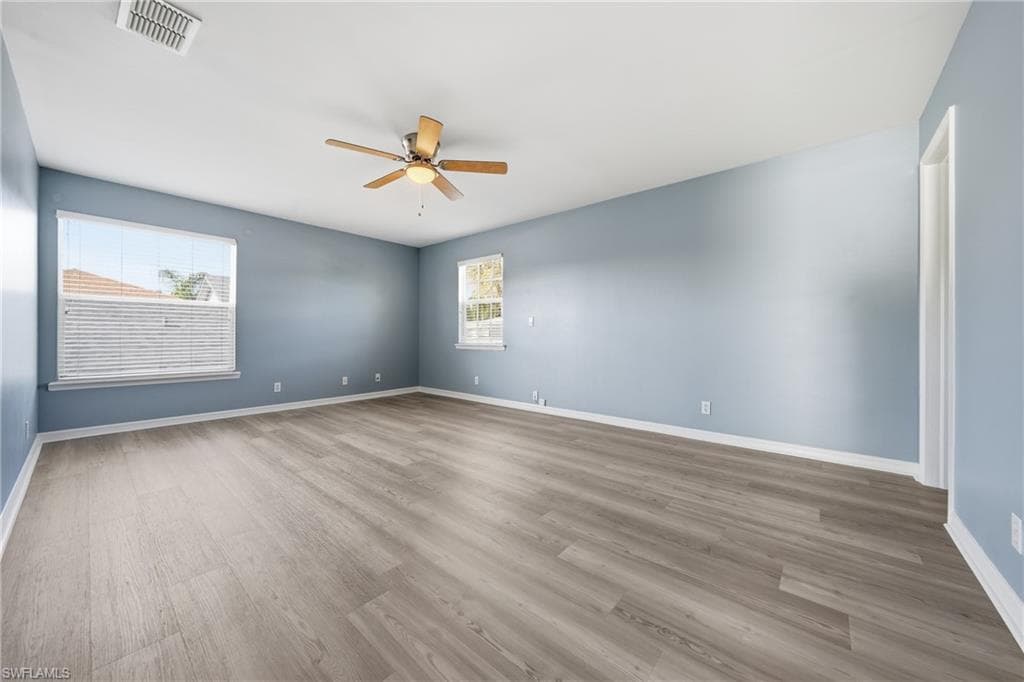 Spacious room featuring light blue walls, wood-finish flooring, and white baseboards