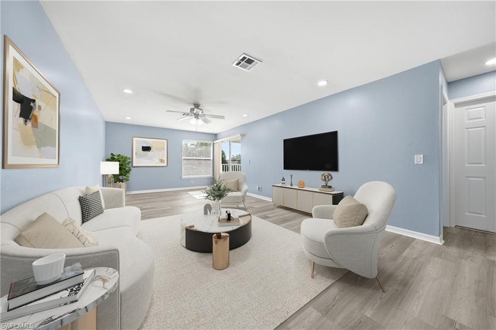 Spacious living area featuring light wood-finish flooring, a ceiling fan with integrated lighting, recessed lighting, and a neutral wall color