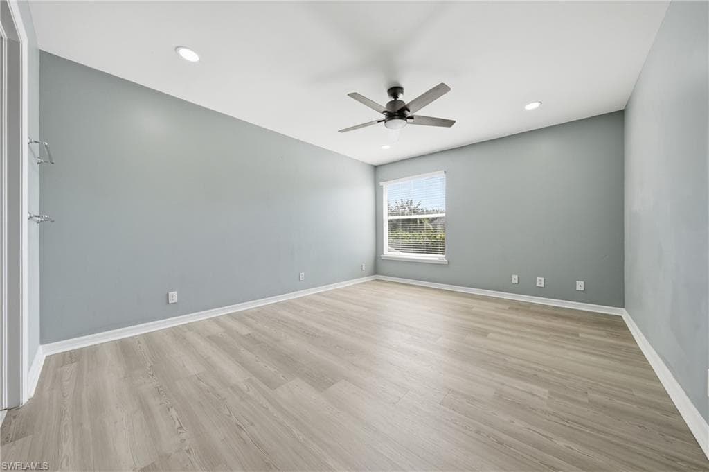 Spacious room featuring light wood-finish flooring, a ceiling fan with integrated lighting, recessed lighting, and a window with blinds
