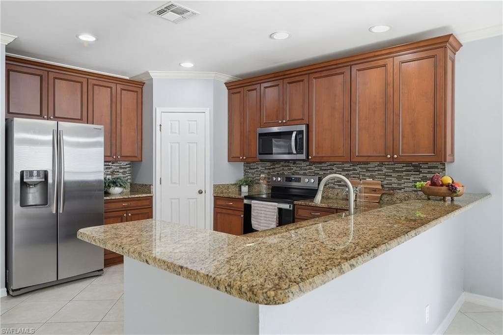 Kitchen featuring a U-shaped countertop with a raised bar, wood cabinetry, stainless steel appliances, and tile flooring