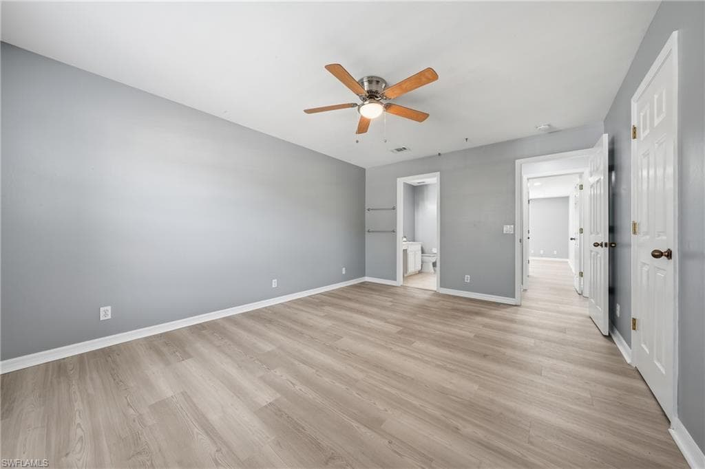 Spacious interior room featuring wood-finish flooring, light gray wall tones, and white baseboards