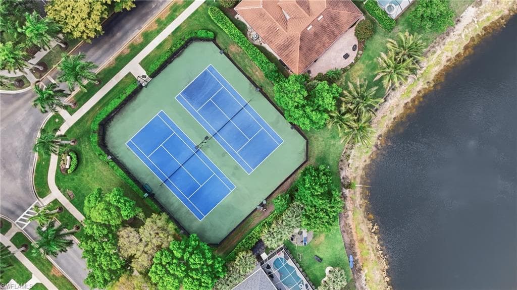 Dual tennis courts with a hard-court surface, surrounded by lush green landscaping and mature trees