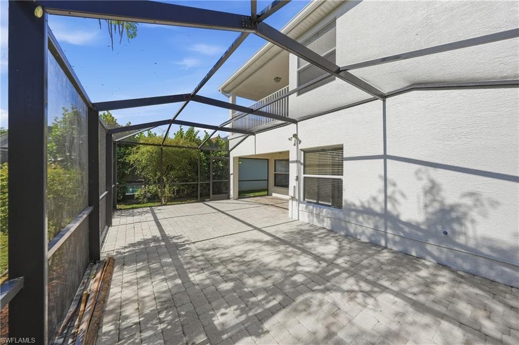 Expansive screened-in patio featuring paver flooring, a white stucco exterior, and a second-story balcony