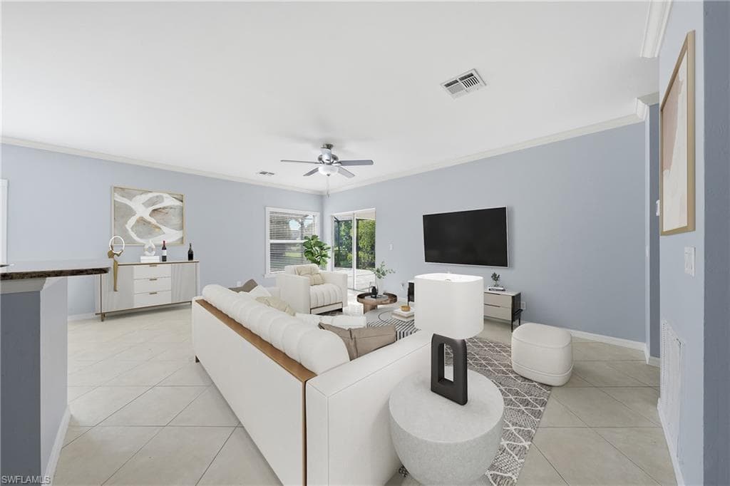 Spacious interior featuring light blue walls, neutral tile flooring, crown molding, and a ceiling fan