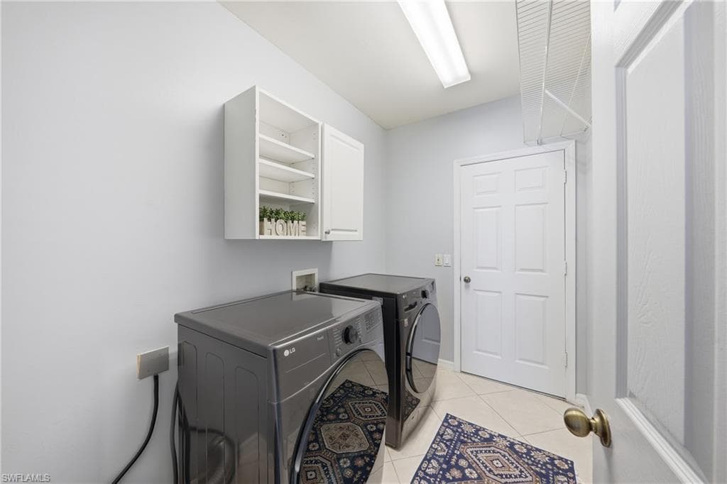 Dedicated laundry area featuring tile flooring, overhead fluorescent lighting, white cabinetry, and a white six-panel door