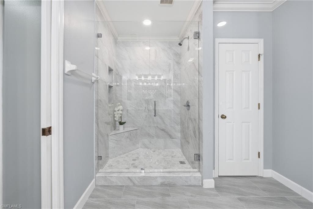 Frameless glass shower enclosure featuring marble-look tile walls, a built-in corner bench, and dual recessed shelves