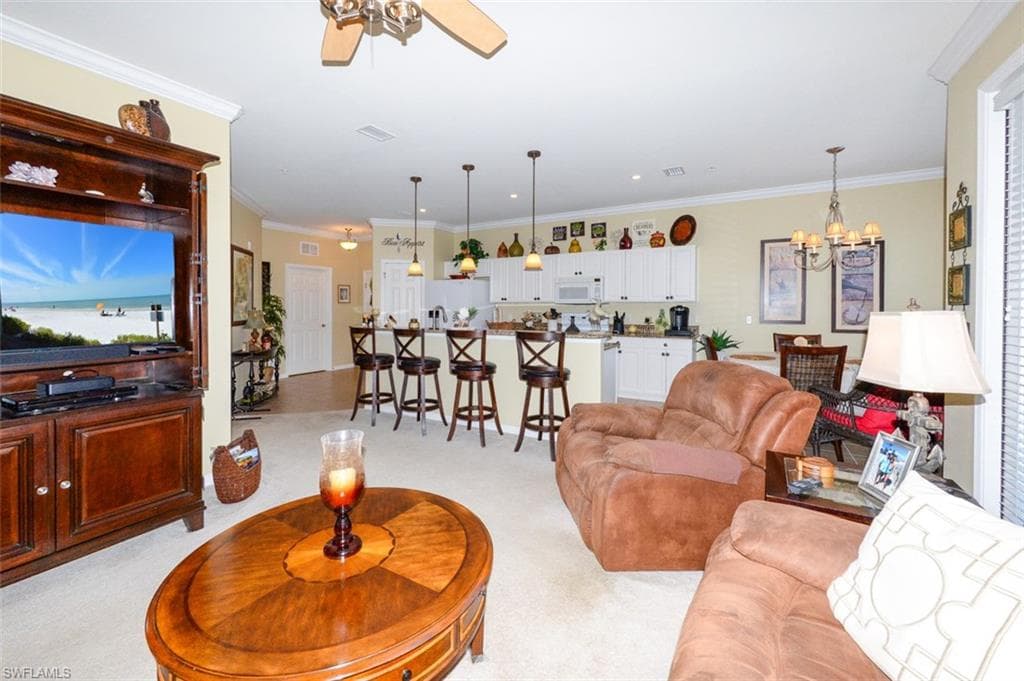 Spacious Great Room features 9'4" ceilings, Crown Molding, Plantation shutters, French door to Lanai and open to the Breakfast bar, dining area and Kitchen. Shows recessed kitchen lighting and pendant lights over breakfast bar.