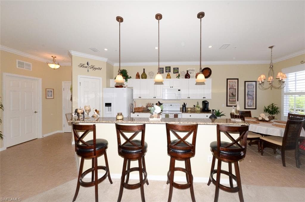 Open Kitchen shows tiled entry foyer to the left and features a Breakfast bar, pantry, 9'4" ceilings, Crown molding, recessed and pendant lighting, White cabinetry, beautiful Granite Countertops, Plantation shutters and Dining area to right.