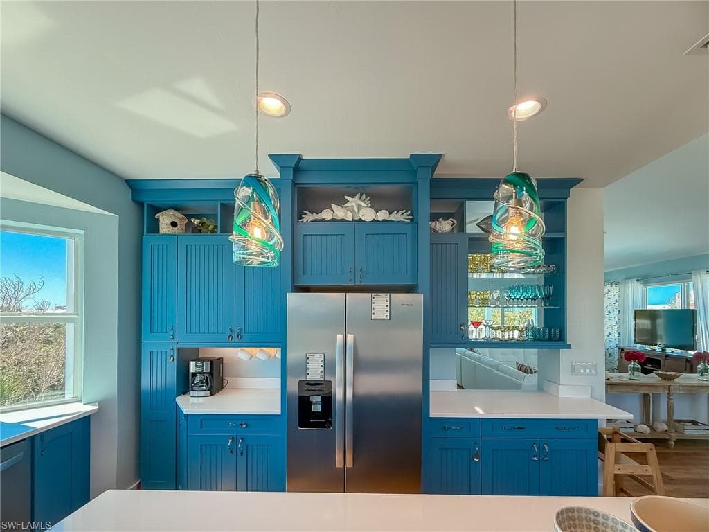 Kitchen with open shelves, blue cabinetry, stainless steel fridge, and pendant lighting