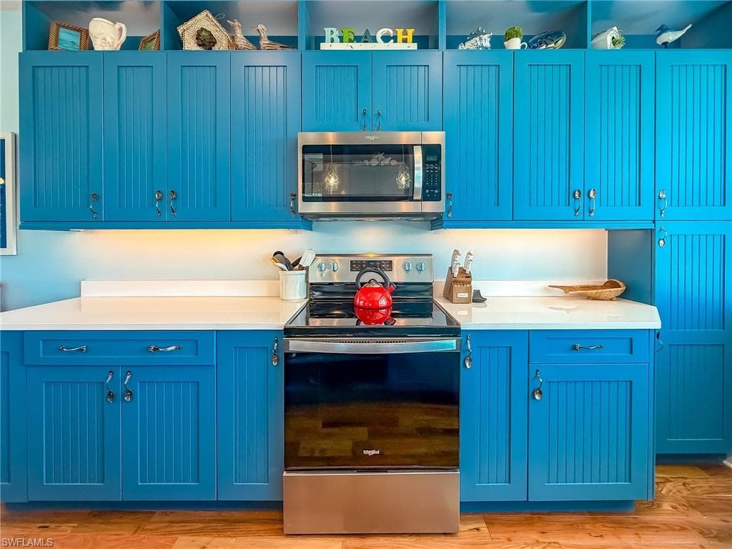Kitchen featuring blue cabinets, light wood finished floors, appliances with stainless steel finishes, and light countertops