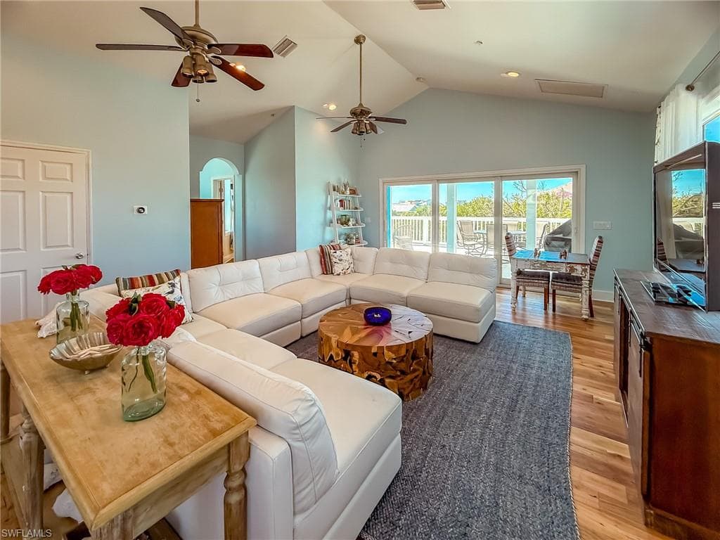 Living room featuring light wood-style flooring, arched walkways, visible vents, and high vaulted ceiling