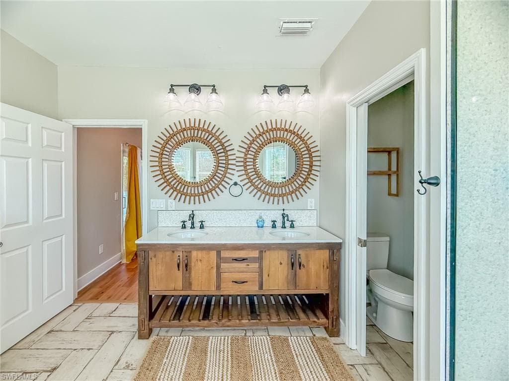 Full bath with double vanity, visible vents, toilet, and a sink