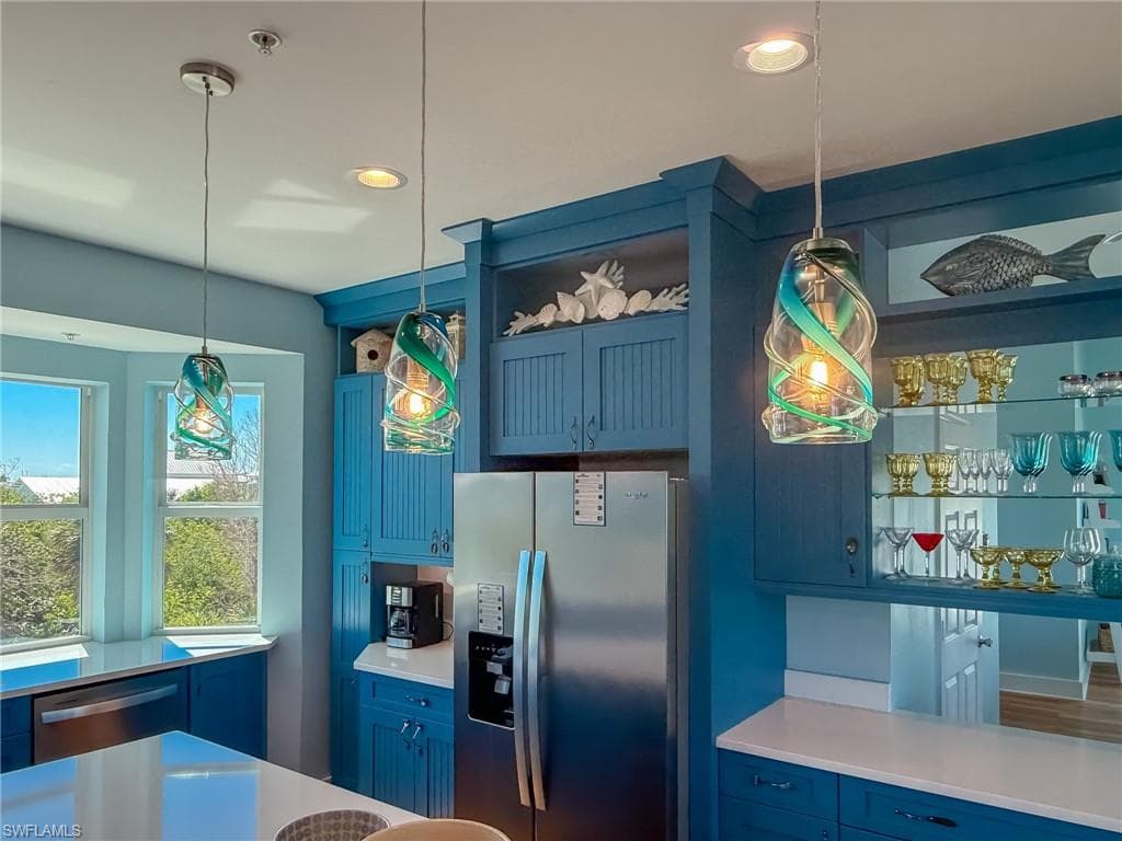 Kitchen with light countertops, blue cabinetry, appliances with stainless steel finishes, and pendant lighting