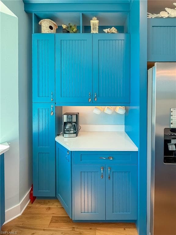Kitchen with baseboards, light countertops, light wood-style floors, stainless steel refrigerator with ice dispenser, and blue cabinets