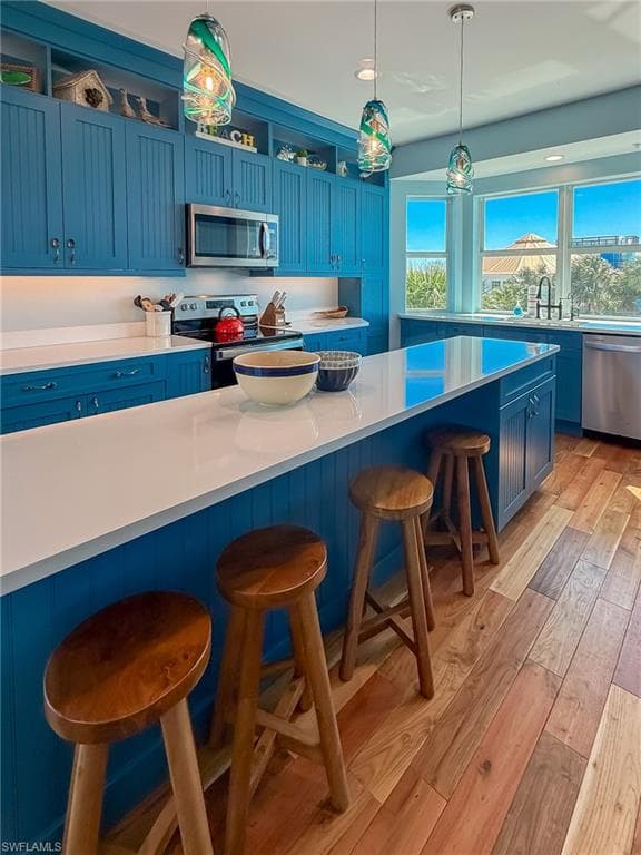 Kitchen featuring blue cabinetry, light wood-style floors, appliances with stainless steel finishes, and a breakfast bar area