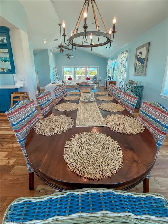 Dining area featuring ceiling fan with notable chandelier, vaulted ceiling, and wood finished floors
