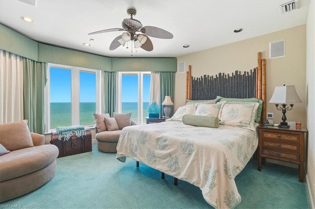 Expansive bedroom featuring a bay window with direct water scenery, light green carpeting, and a ceiling fan with integrated lighting