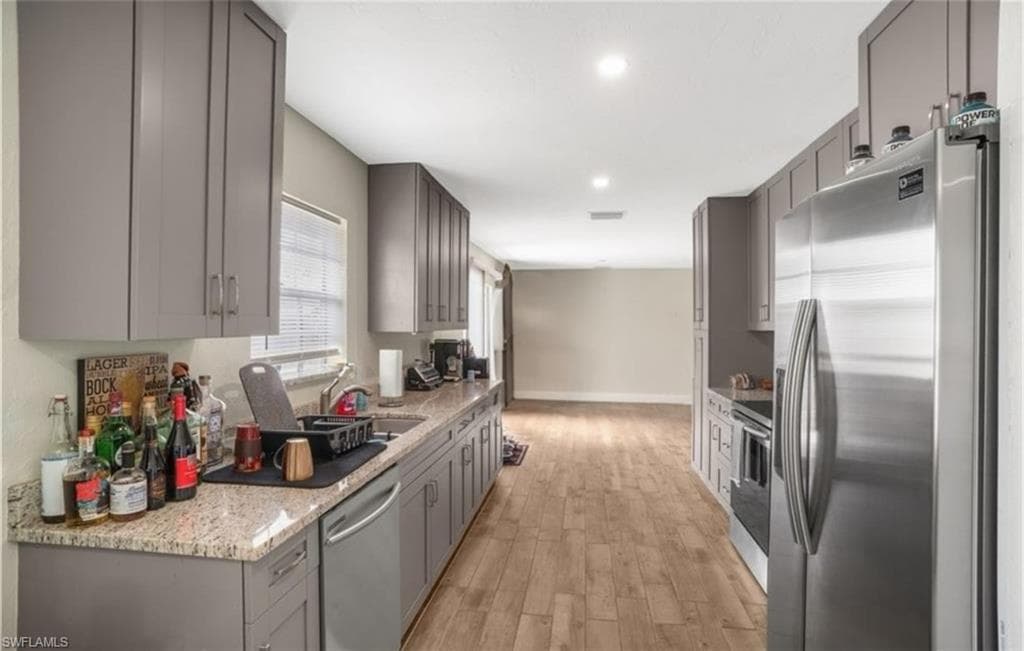 Kitchen featuring gray cabinets, appliances with stainless steel finishes, light stone counters, light wood finished floors, and recessed lighting