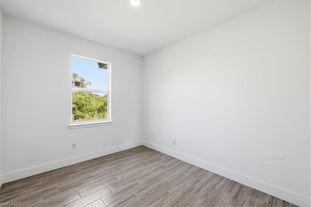 Bright interior space featuring a window with exterior foliage, white walls, white baseboards, and plank-style flooring