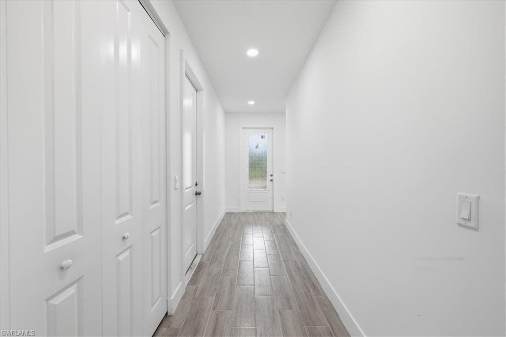 Hallway featuring wood-finish flooring, recessed lighting, white walls, and white panel doors
