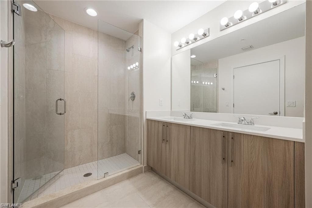 Bathroom with tile patterned floors, a sink, double vanity, and a stall shower