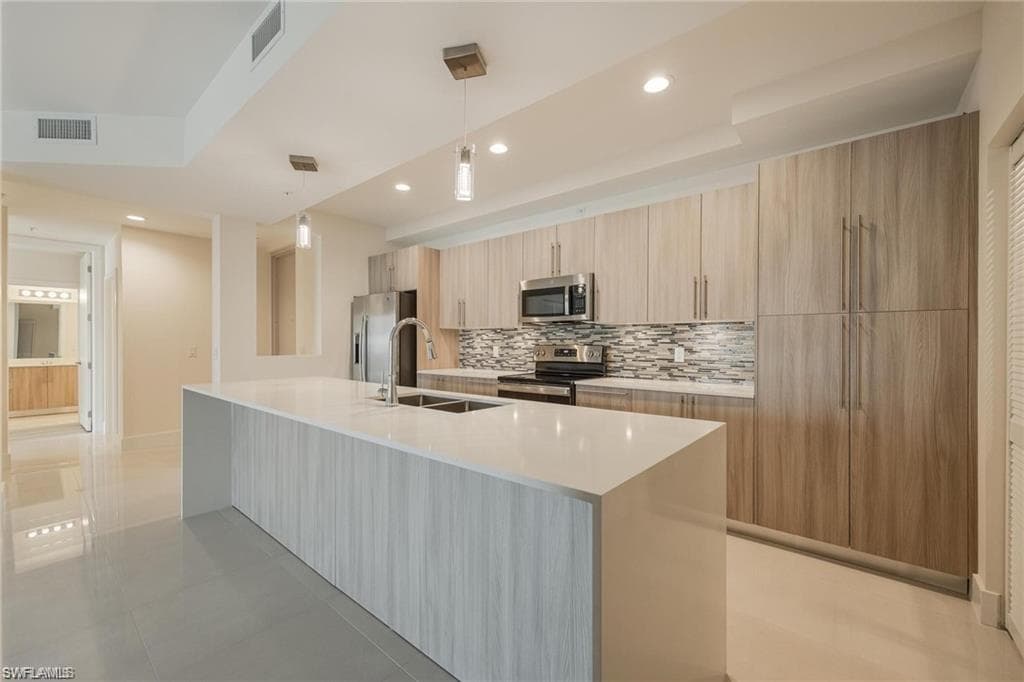 Kitchen with a sink, decorative backsplash, modern cabinets, stainless steel appliances, and visible vents