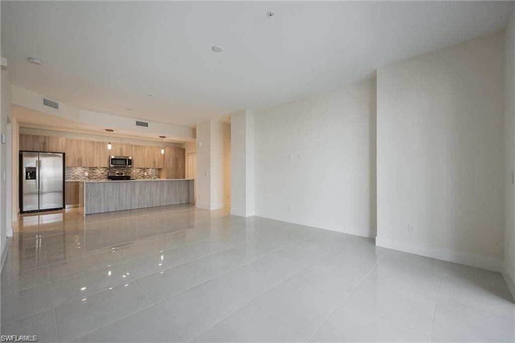 Unfurnished living room featuring baseboards, visible vents, and light tile patterned floors