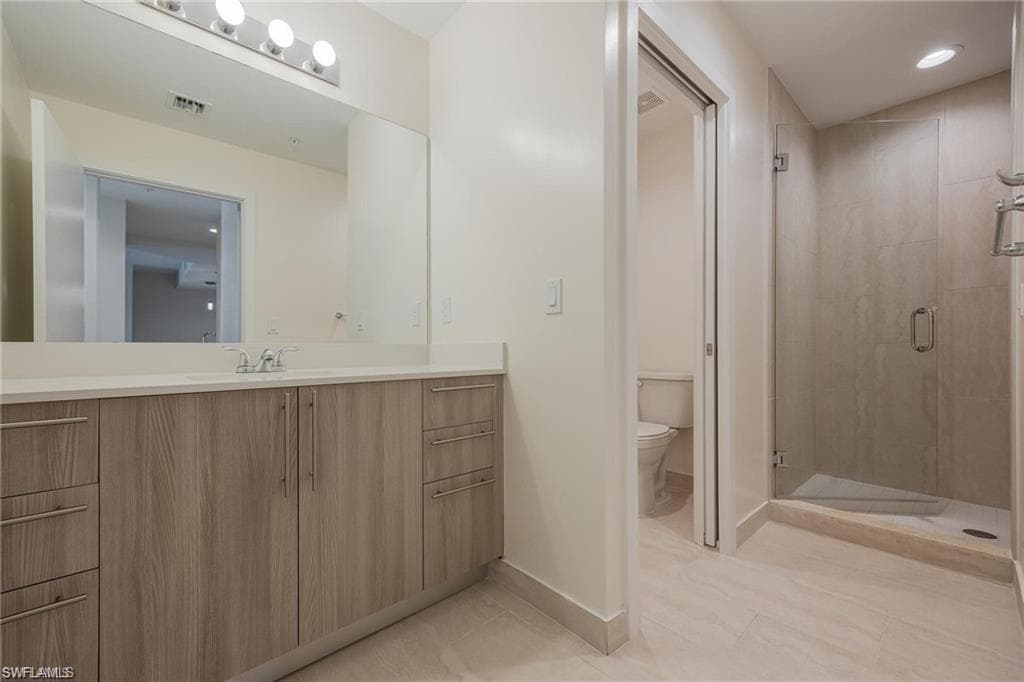 Bathroom with a shower stall, tile patterned floors, vanity, baseboards, and toilet